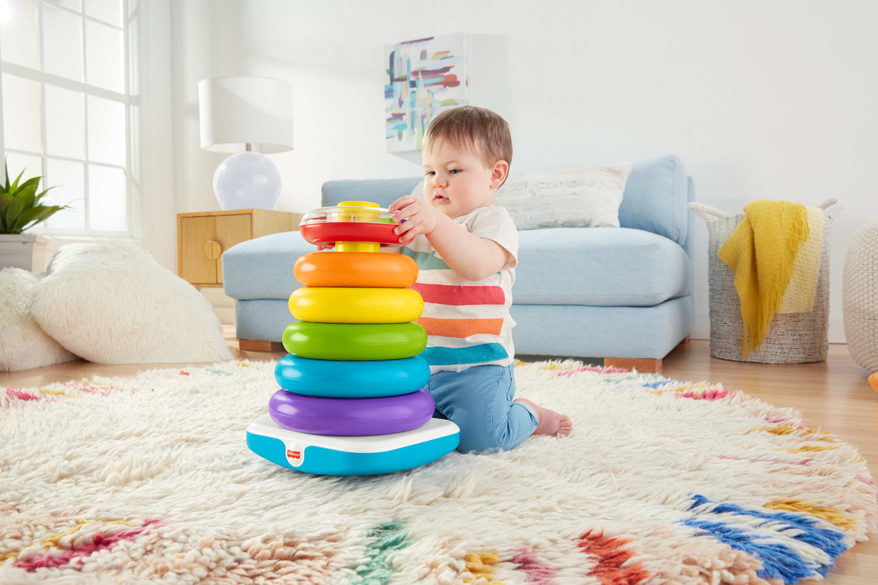 Ein Baby spielt mit einem bunten Stapelring-Spielzeug auf einem Teppich.