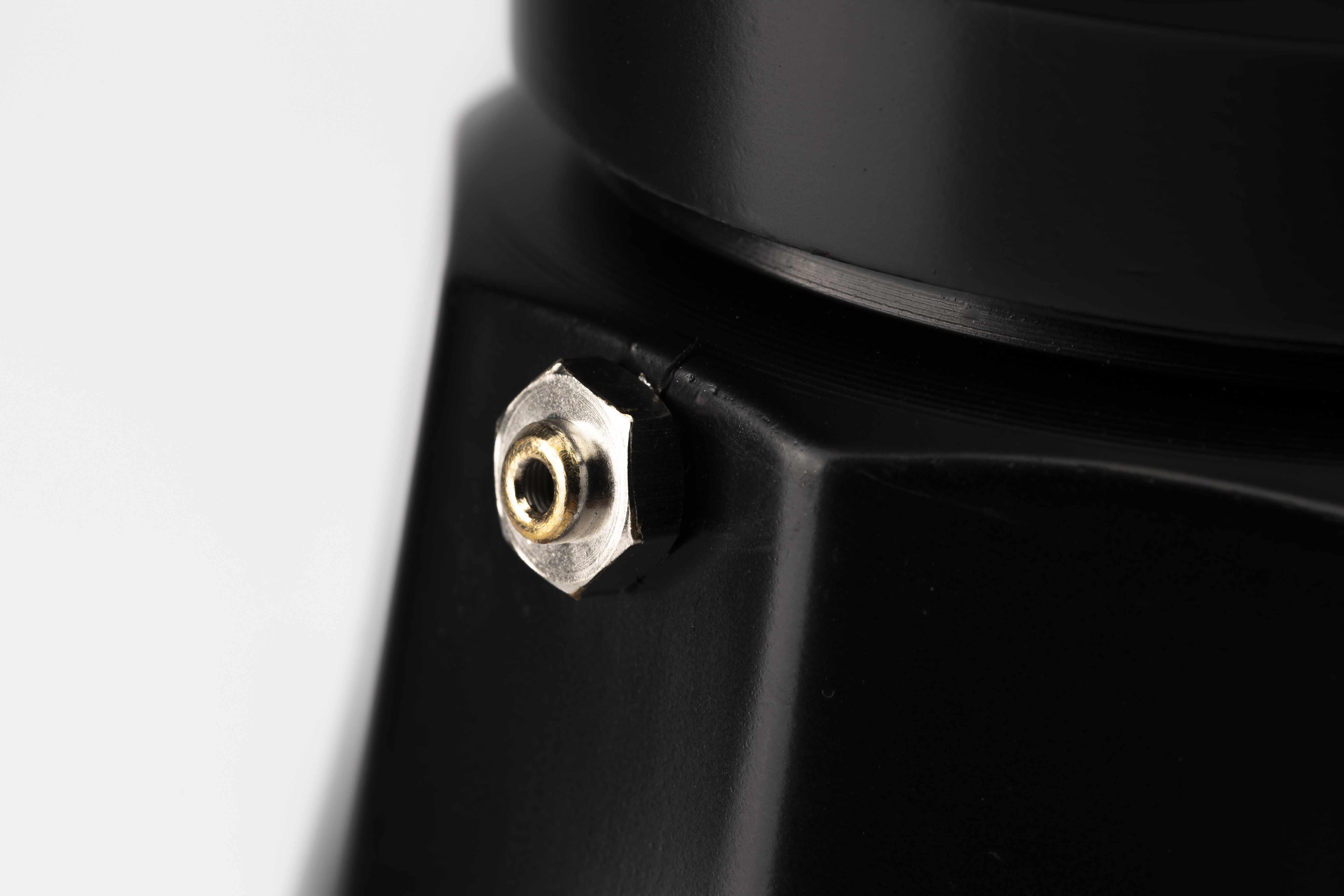 Un perno hexagonal plateado con inserción roscada dorada en objeto negro.
