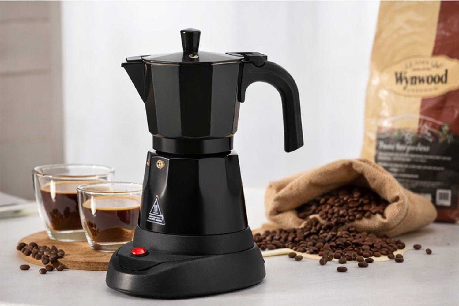 Cafetera negra con dos vasos de café y granos de café.
