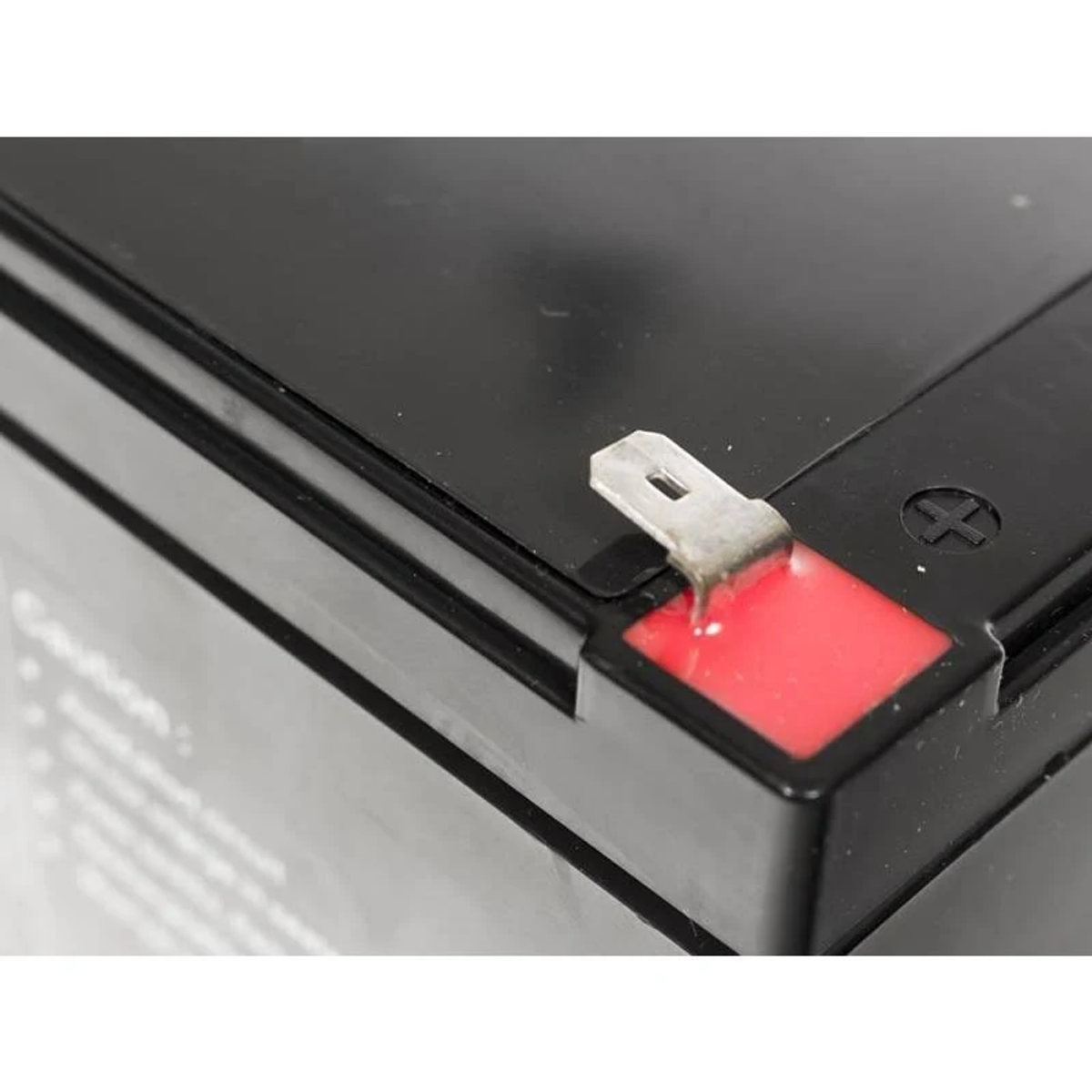 Primer plano de una batería negra con terminal positivo rojo y conector metálico.