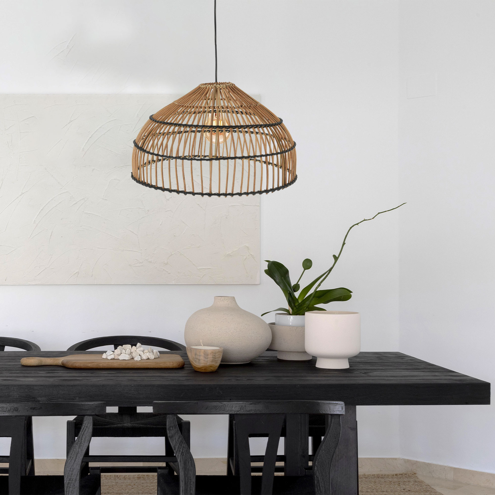 Una mesa de madera negra con decoraciones: jarrón, vela, planta y piedras.
