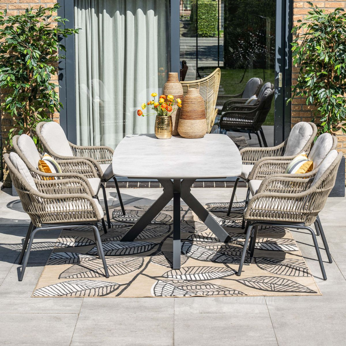 Een buitenset met eettafel en vier stoelen op een terras, versierd met vazen en bloemen.