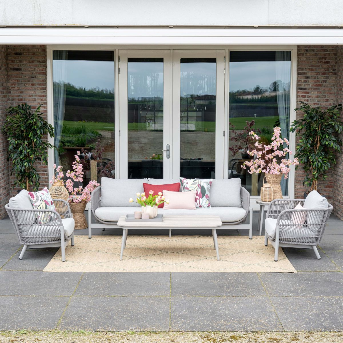 Outdoor furniture set with sofa, armchairs, coffee table and rug on a patio.