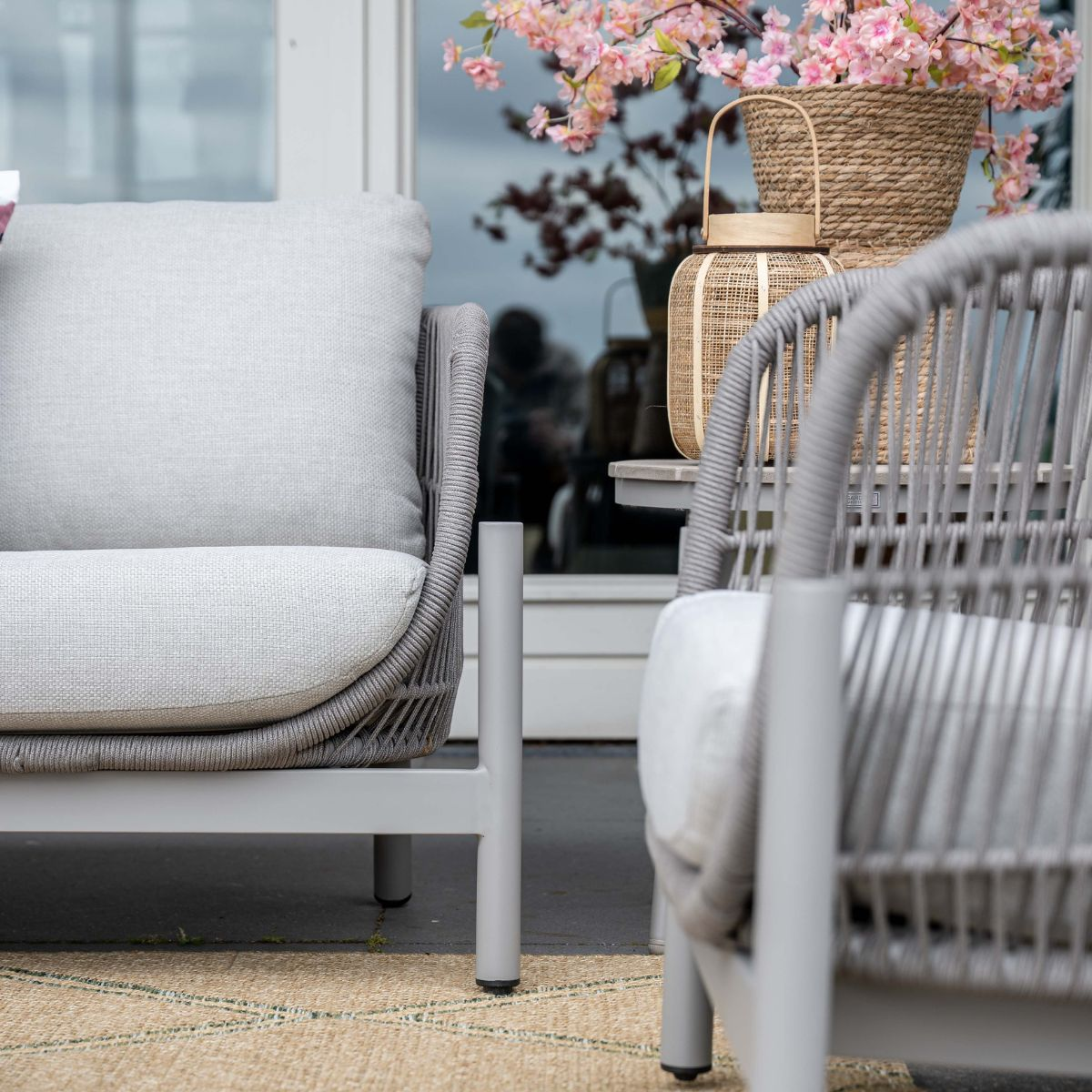 Gray rattan armchairs with cushions, basket, and lantern before a window.