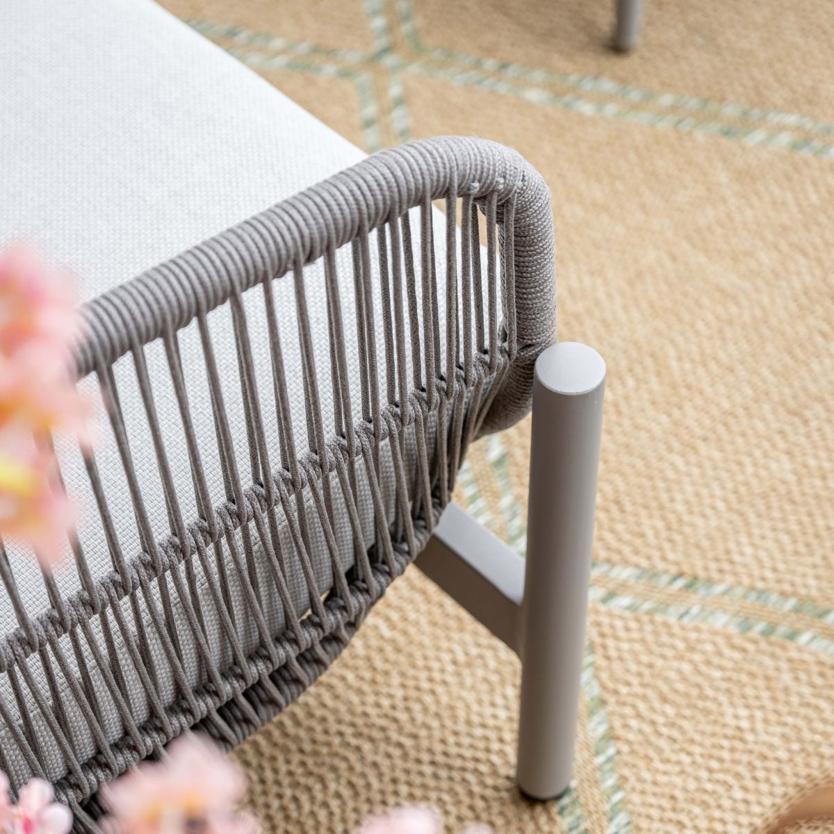 Gray rattan armchair with white cushion on a beige rug.