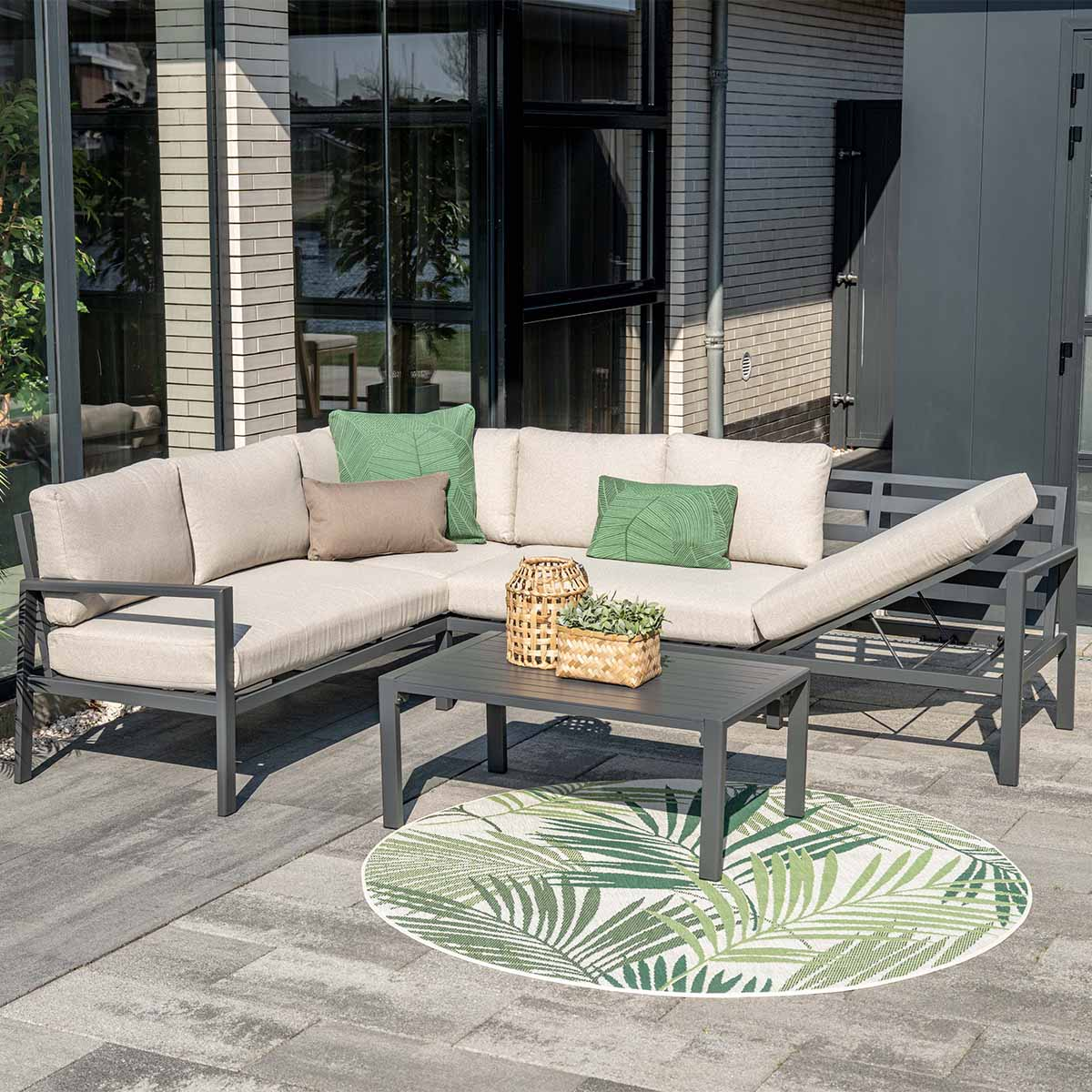 A sectional sofa with cushions and a table on a patio with a palm leaf patterned rug.