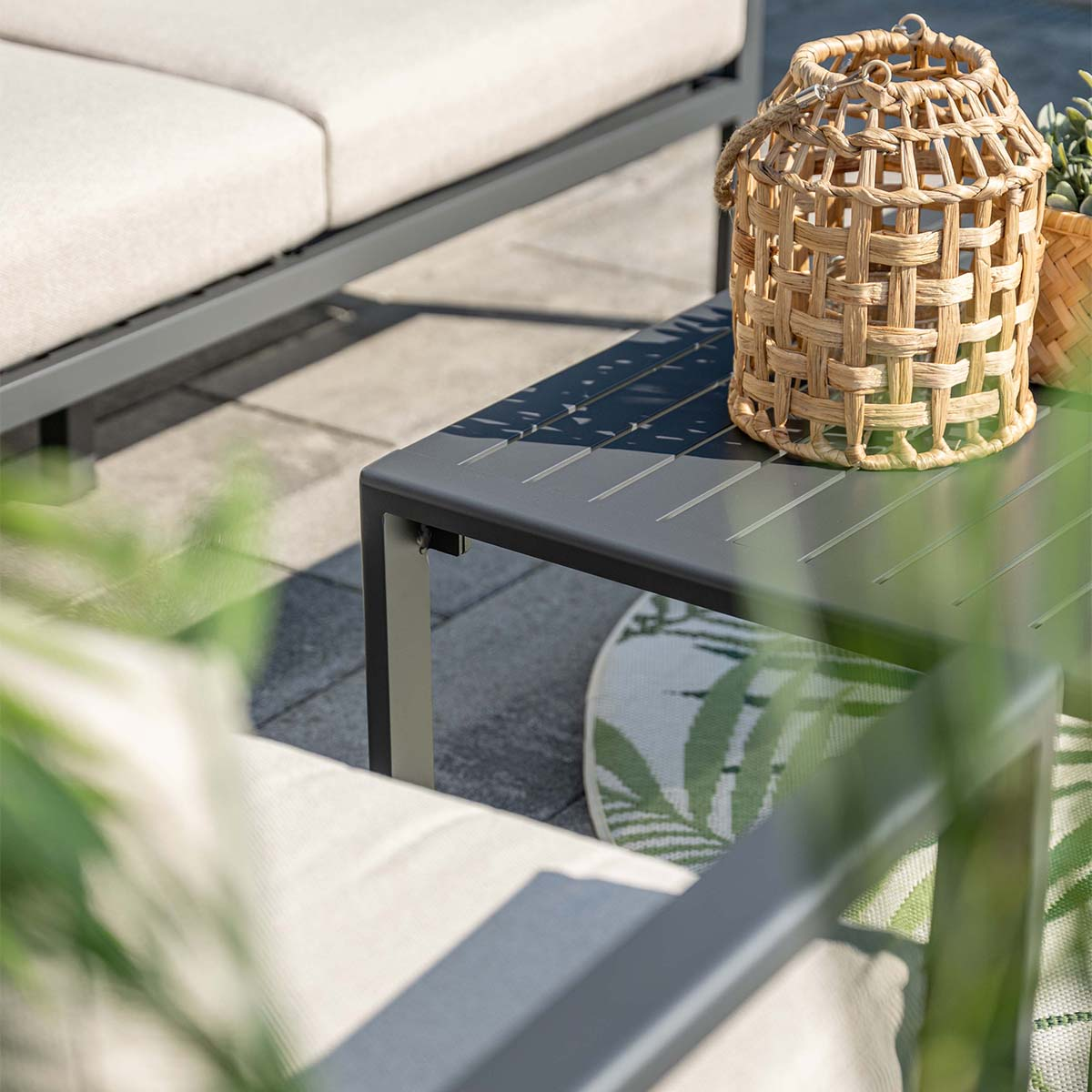 Gray table with wicker basket and cushions on a stone patio.