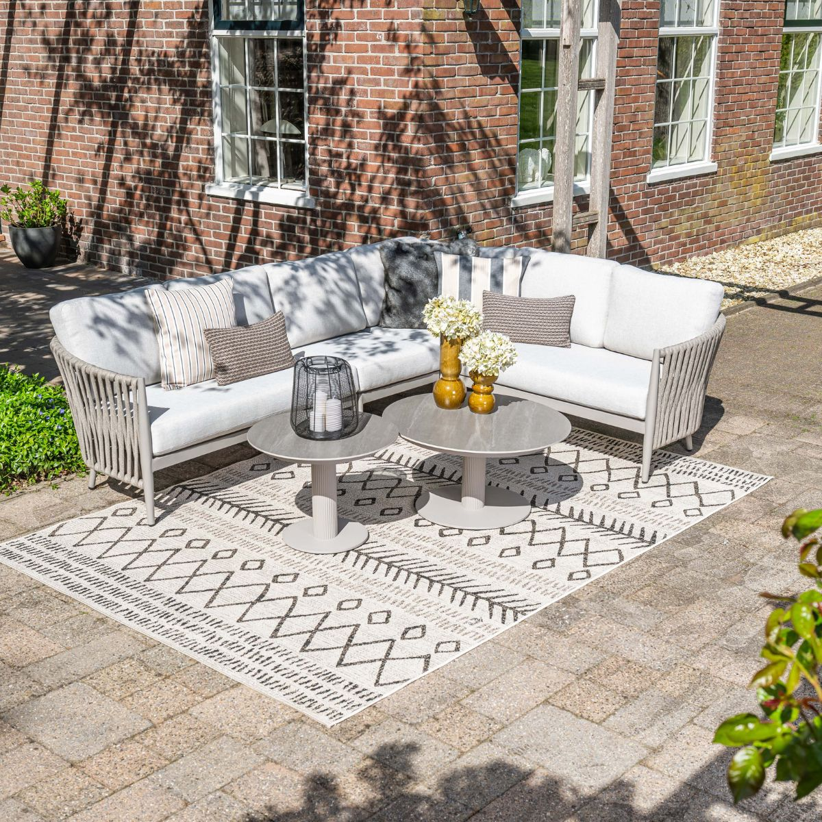 Gray outdoor sofa set with cushions on a rug in front of a brick wall.
