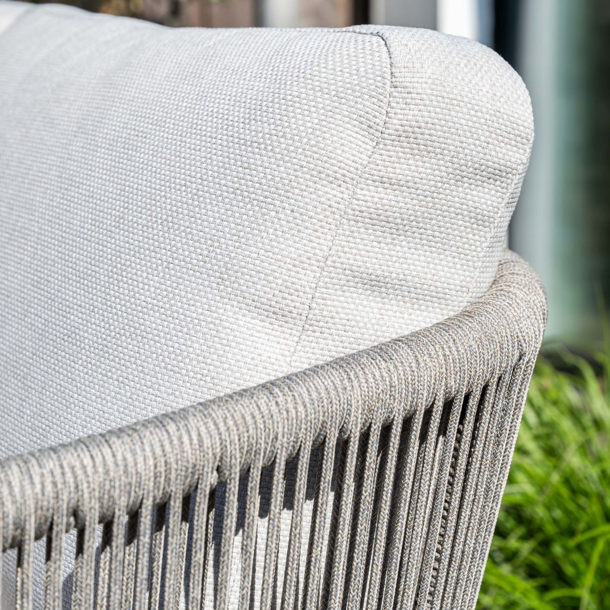 Close-up of a light gray cushion on a gray rope chair, with green grass in background.