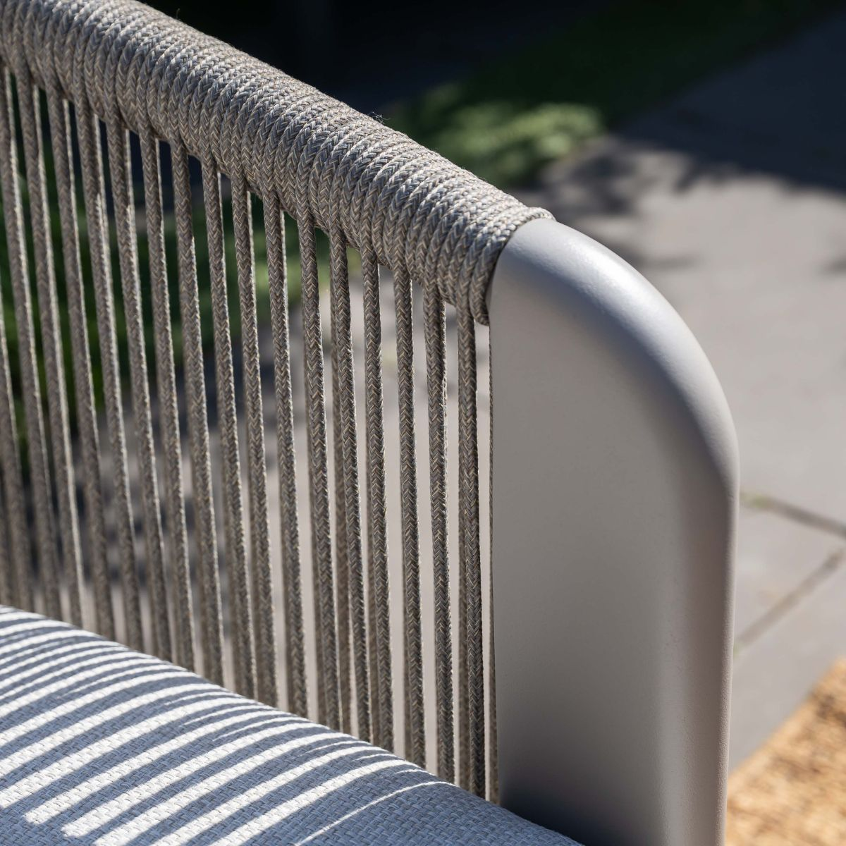Close-up of a grey chair frame with rope detailing and a striped cushion.