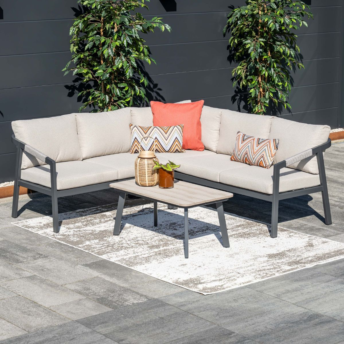 Sectional sofa with beige cushions, coffee table, and plants against a dark wall.