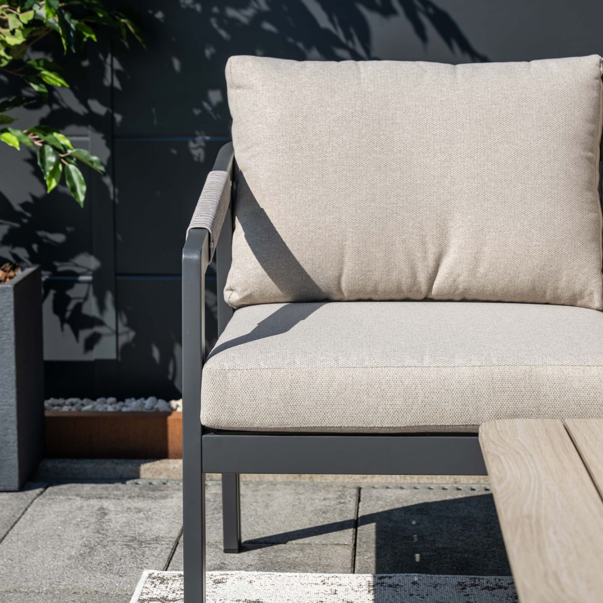 Gray outdoor chair with beige cushions on a stone patio.