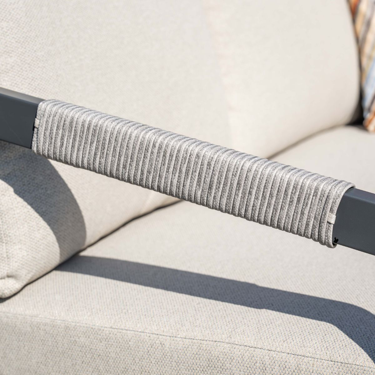 Gray rope armrest cover on a light sofa with shadows.