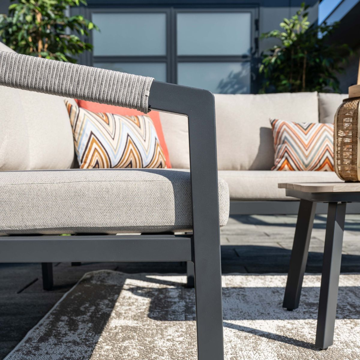A modern outdoor chair with grey cushions and decorative pillows on a patio.