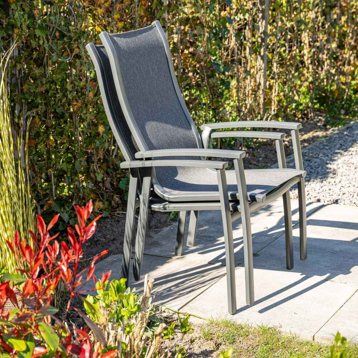 Twee grijze buitenstoelen met stoffen zitting op een stenen terras.