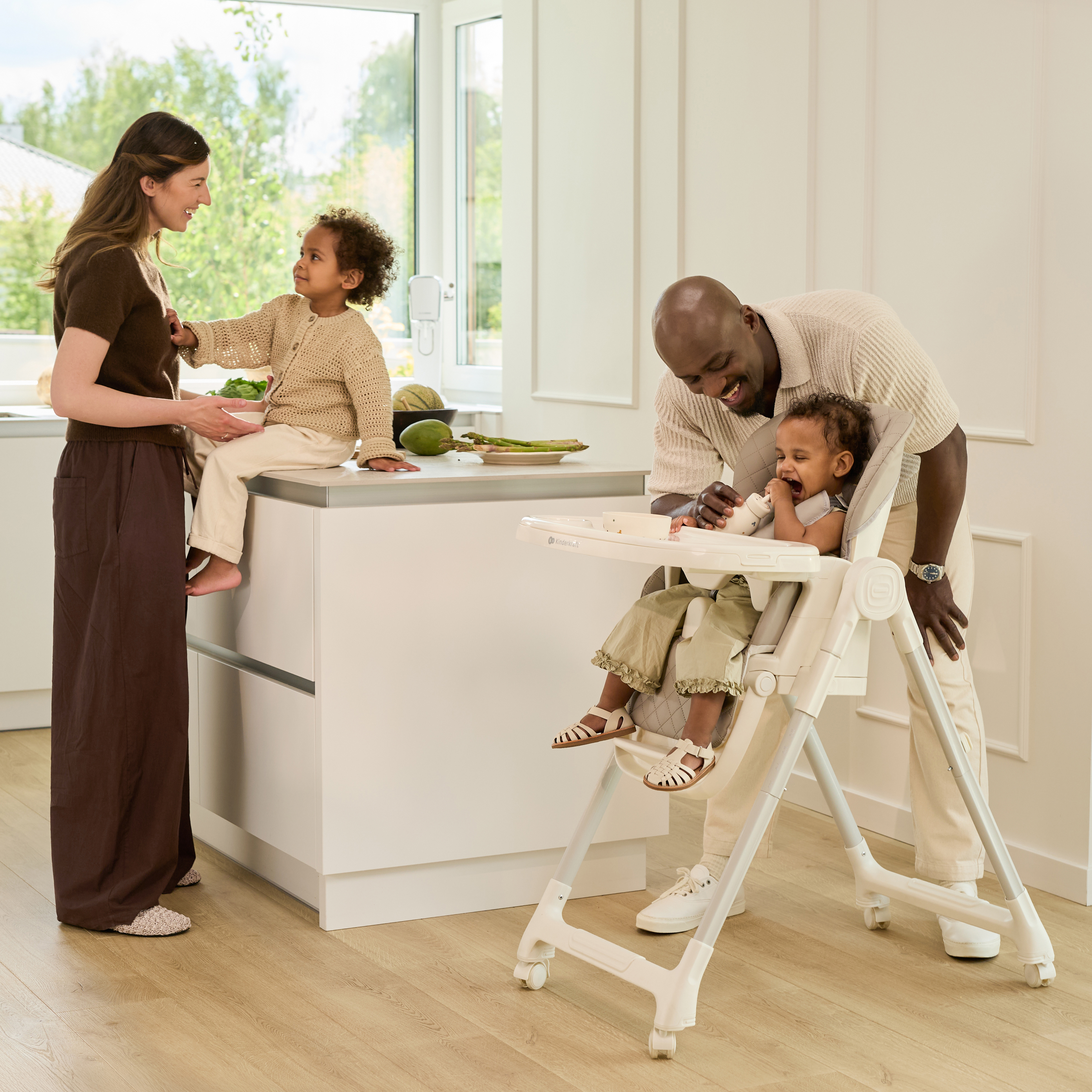 Eine Familie genießt die Zeit in der hellen Küche. Ein Kind sitzt auf der Arbeitsplatte, ein anderes im Hochstuhl.