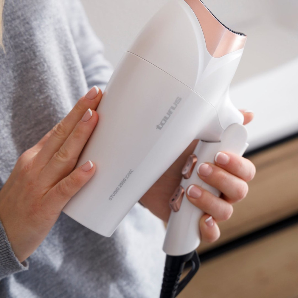 Osoba trzyma białą suszarkę do włosów z różowo-złotymi akcentami.