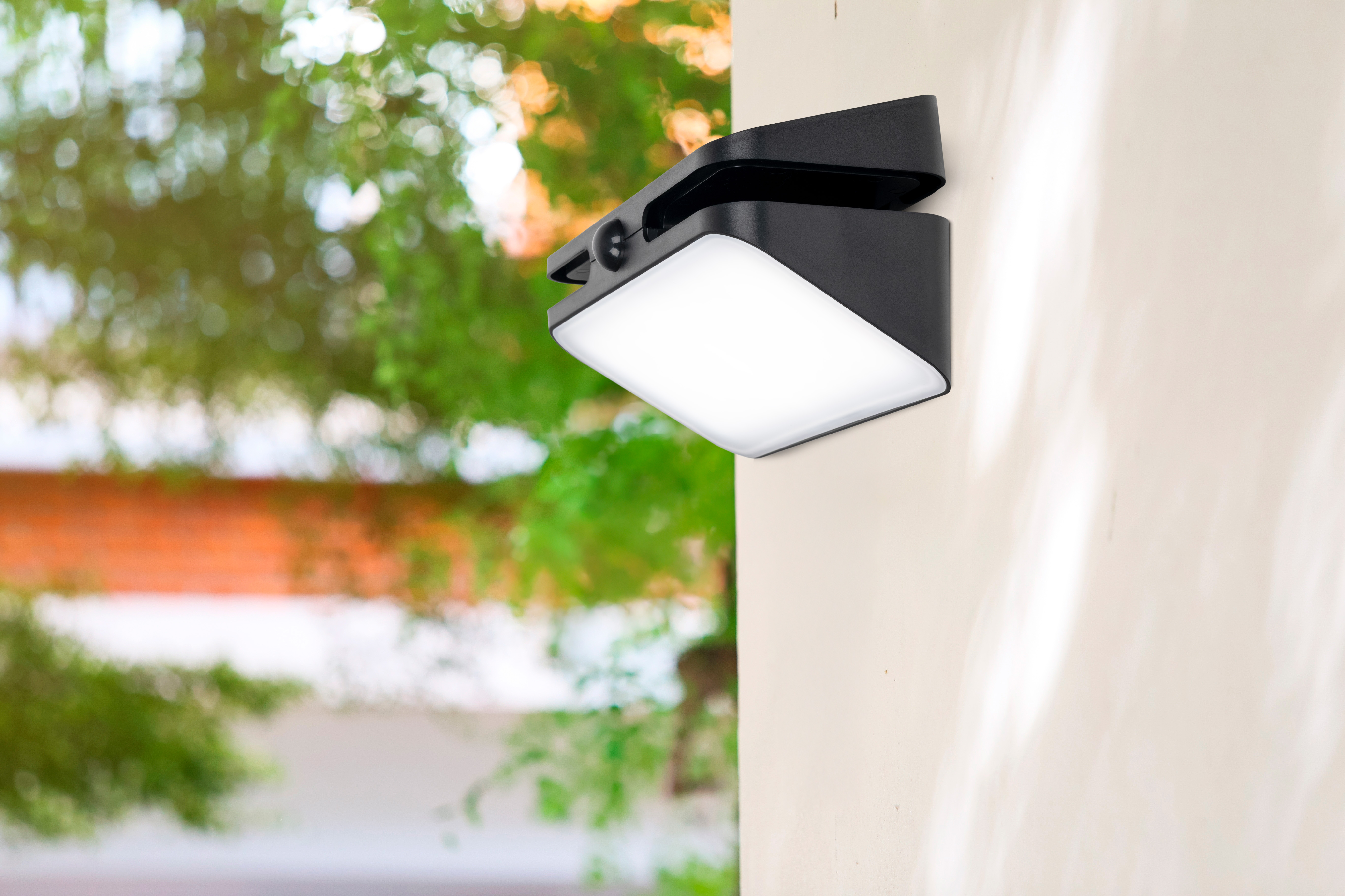 Eine schwarze Wandleuchte mit Bewegungsmelder leuchtet auf einer cremefarbenen Wand.