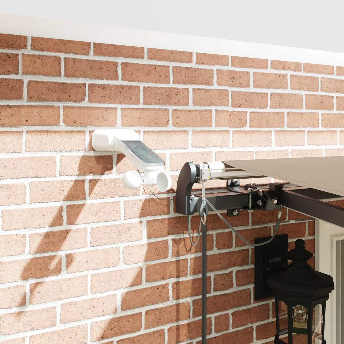 Ein weißes Wettergerät mit Solarpanel an einer Ziegelwand neben einem Markisenarm und einer Lampe.