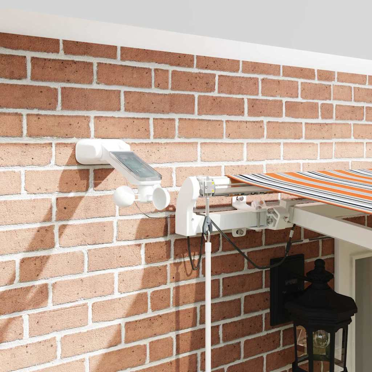 Weiße Wetterstation mit Solarpanel an Ziegelwand, daneben eine Markise.