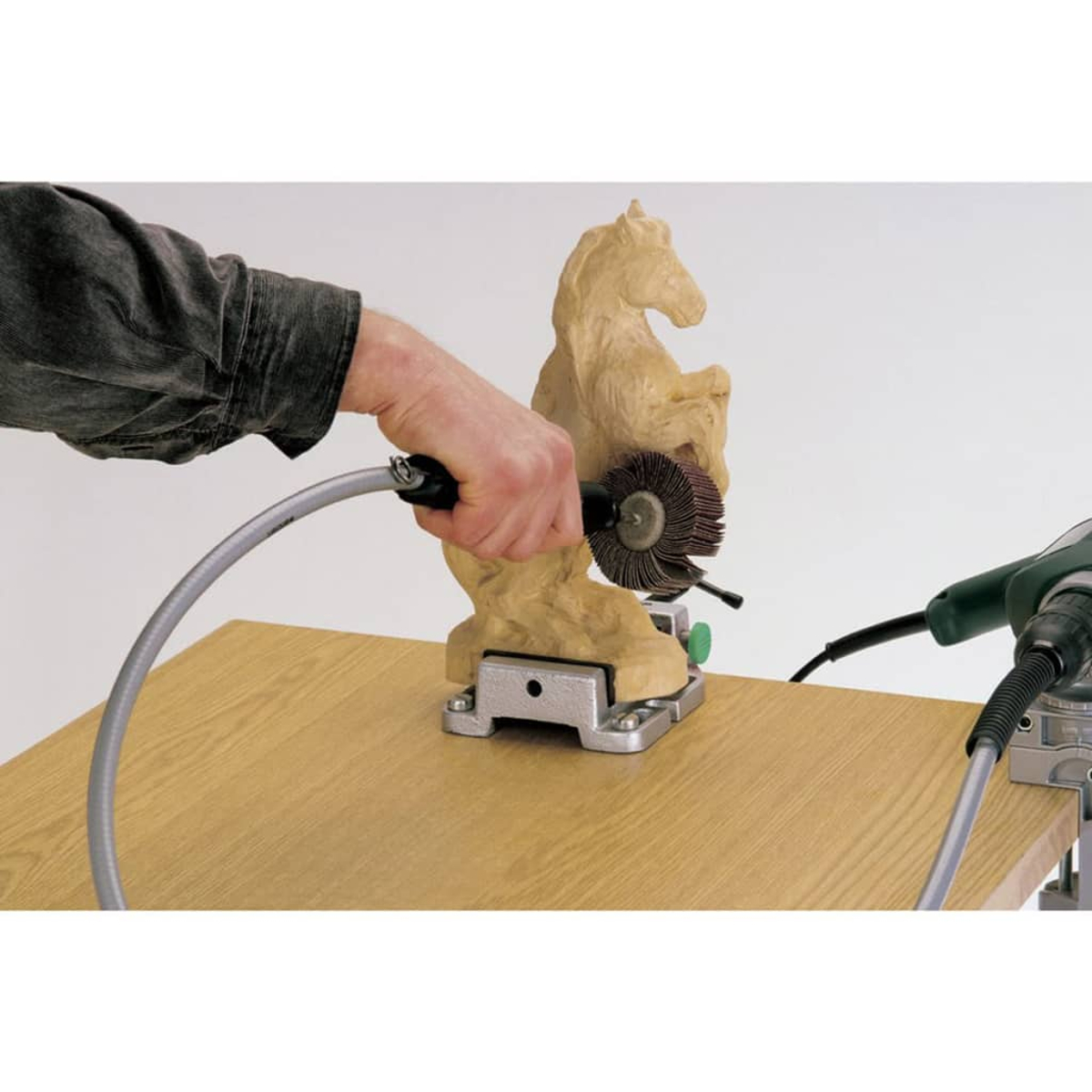 Una mano trabaja en una escultura de caballo de madera con una herramienta de cepillo giratorio.