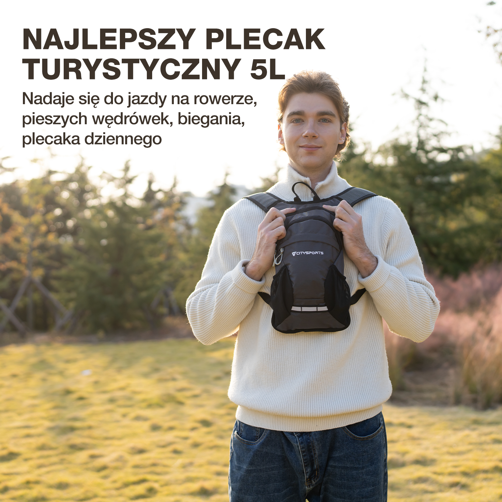 Mężczyzna w białym swetrze i dżinsach trzyma mały szary plecak.