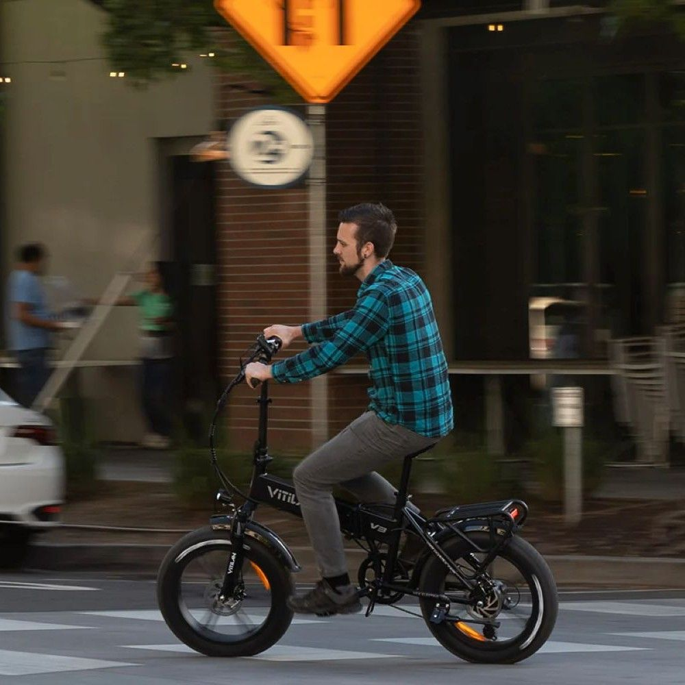 Un hombre monta una bicicleta eléctrica negra en una calle con camisa a cuadros.