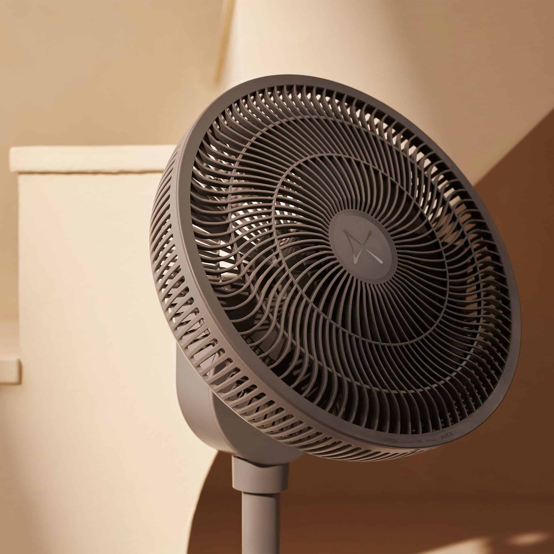 Ein grauer Standventilator mit einem runden Gitter steht vor einem cremefarbenen Hintergrund.