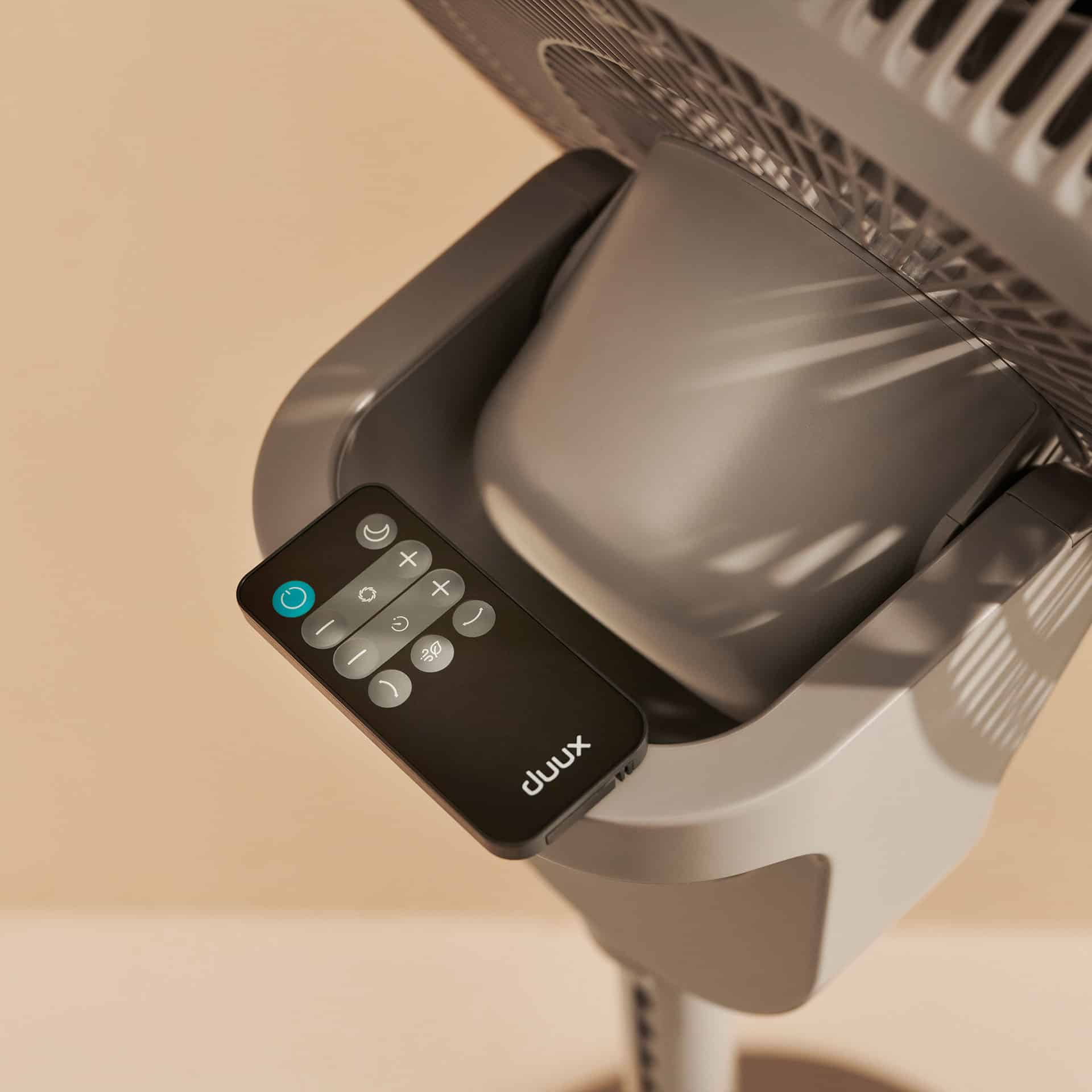 Graue Fernbedienung mit Knöpfen liegt auf einem Ventilator.