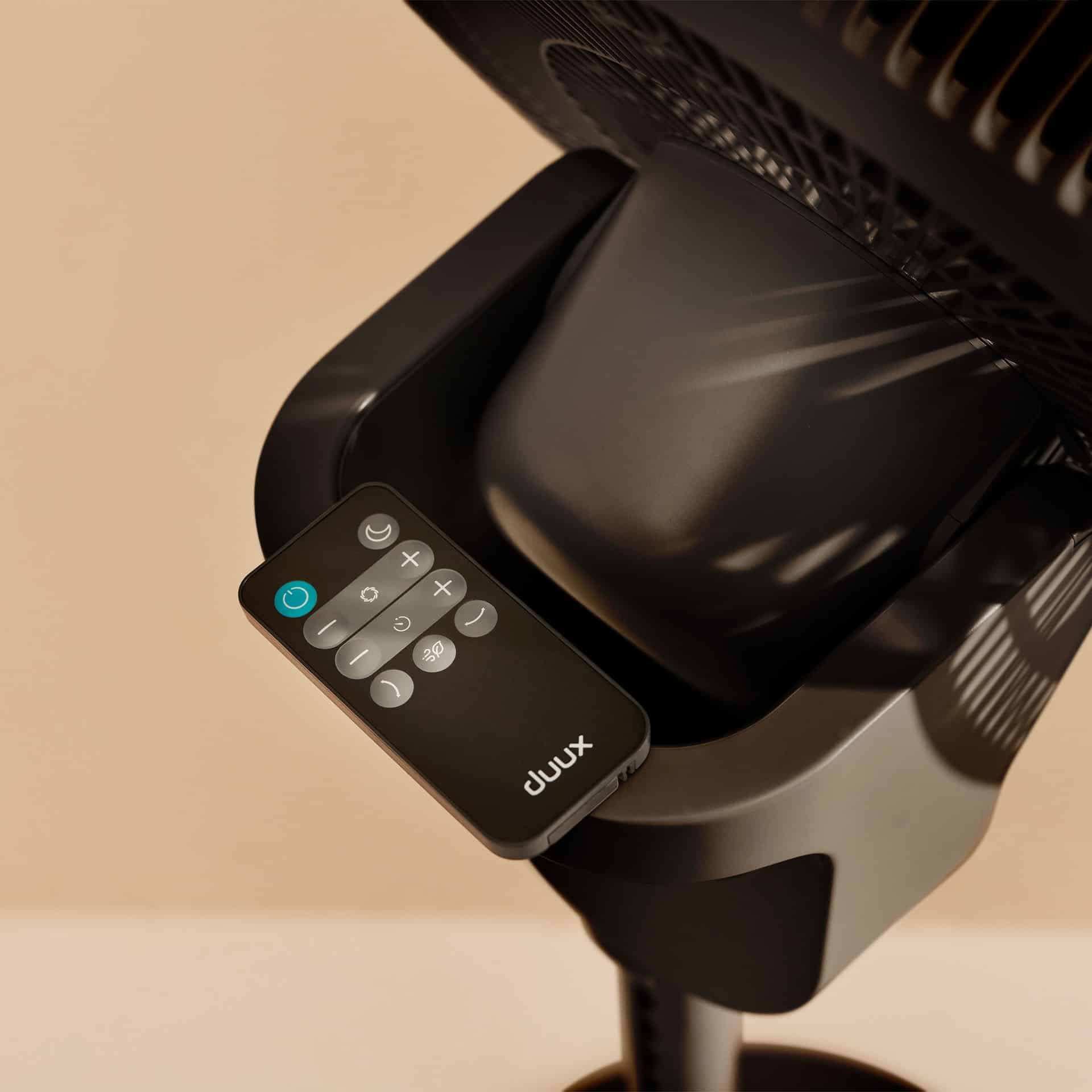 Télécommande noire avec boutons sur un pied de ventilateur.