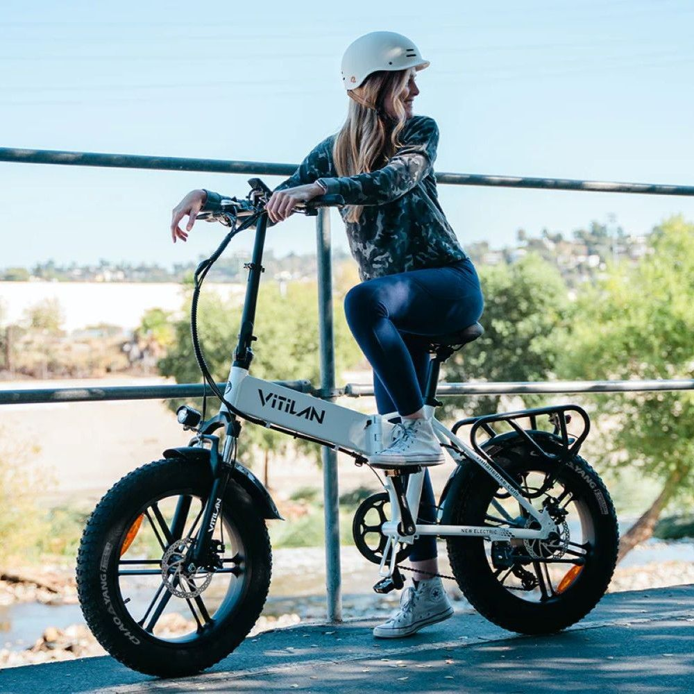 Una mujer con casco se sienta en una bicicleta eléctrica blanca con llantas anchas.