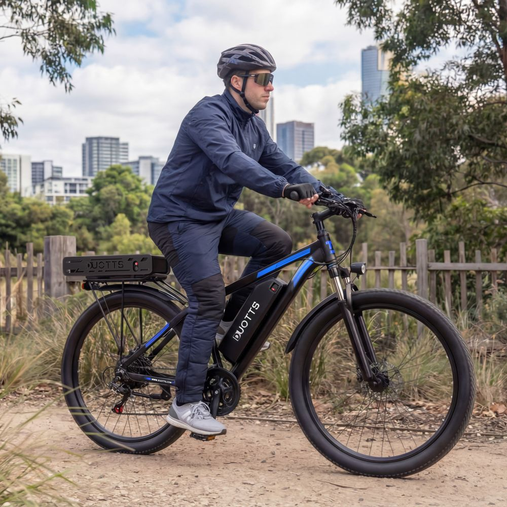 Uomo in giacca blu guida e-bike su sentiero sterrato, skyline cittadino sullo sfondo.