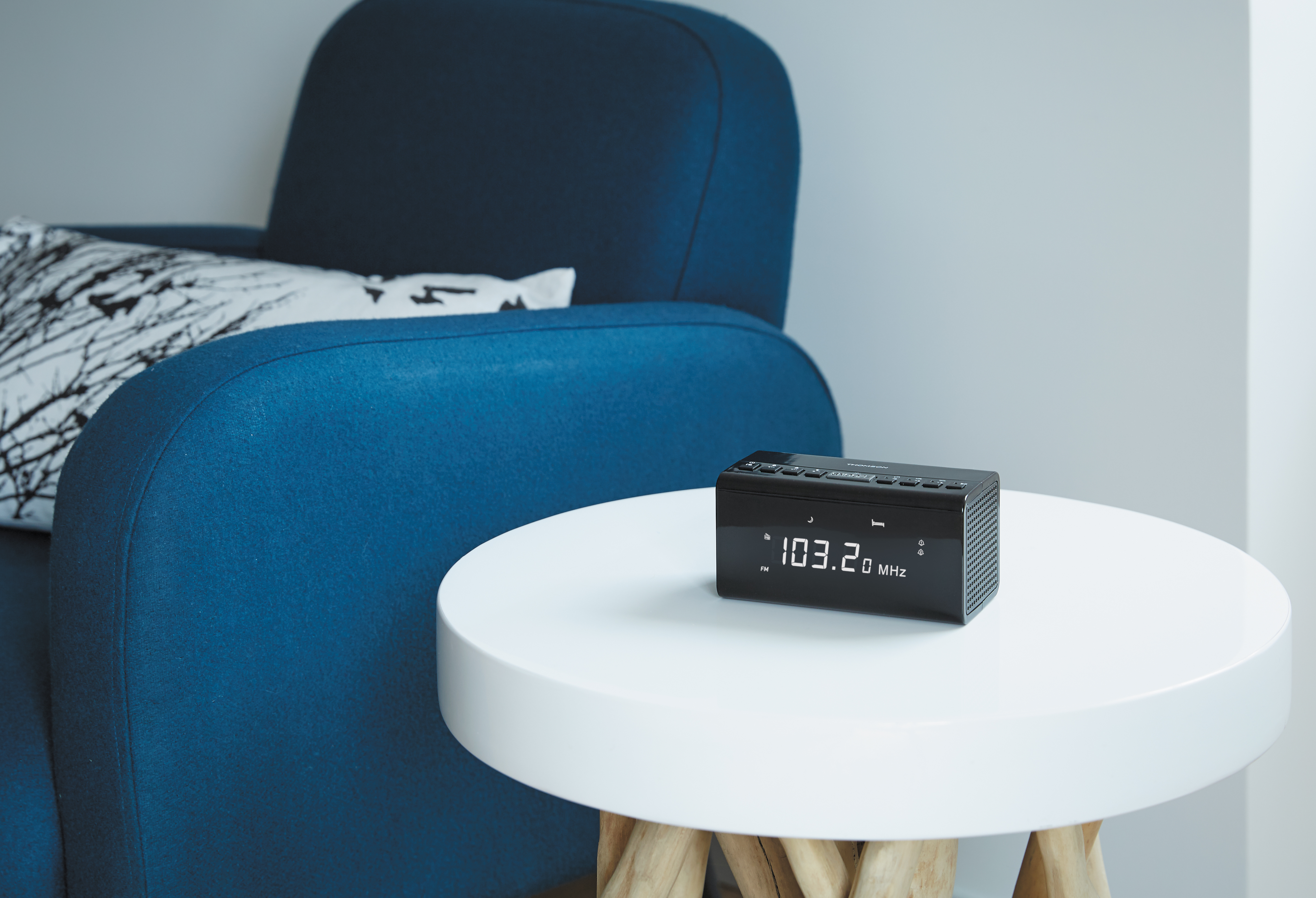 Czarny radiobudzik na białym stole obok niebieskiego fotela.