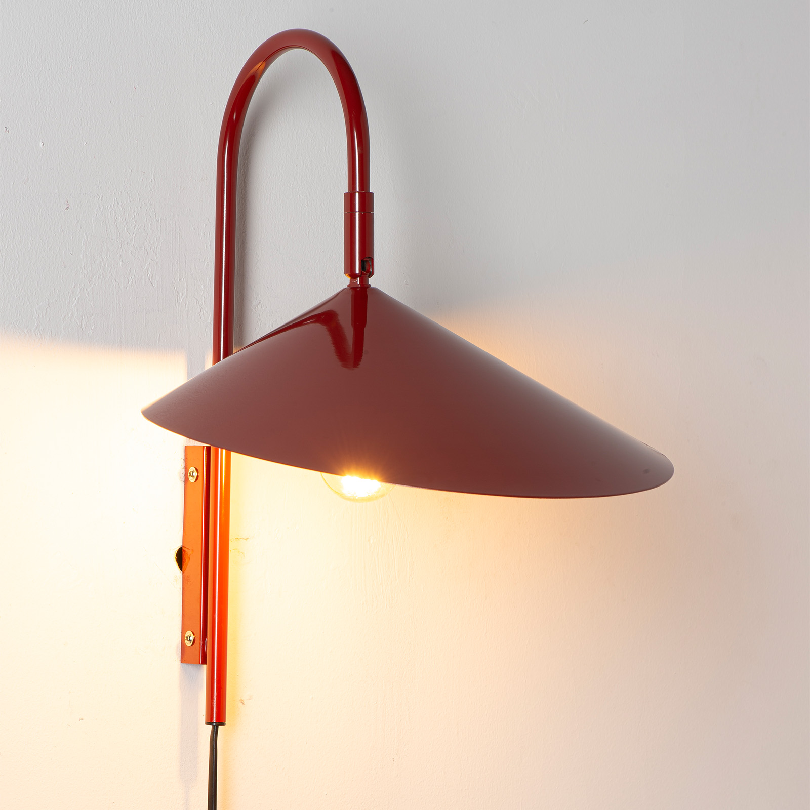 Una lámpara de pared roja con brazo curvo y pantalla cónica.