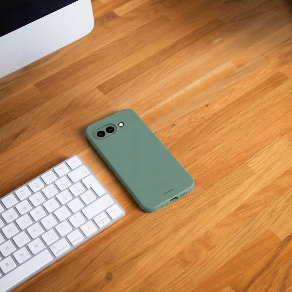 Zielone etui na telefon obok białej klawiatury na drewnianym biurku.