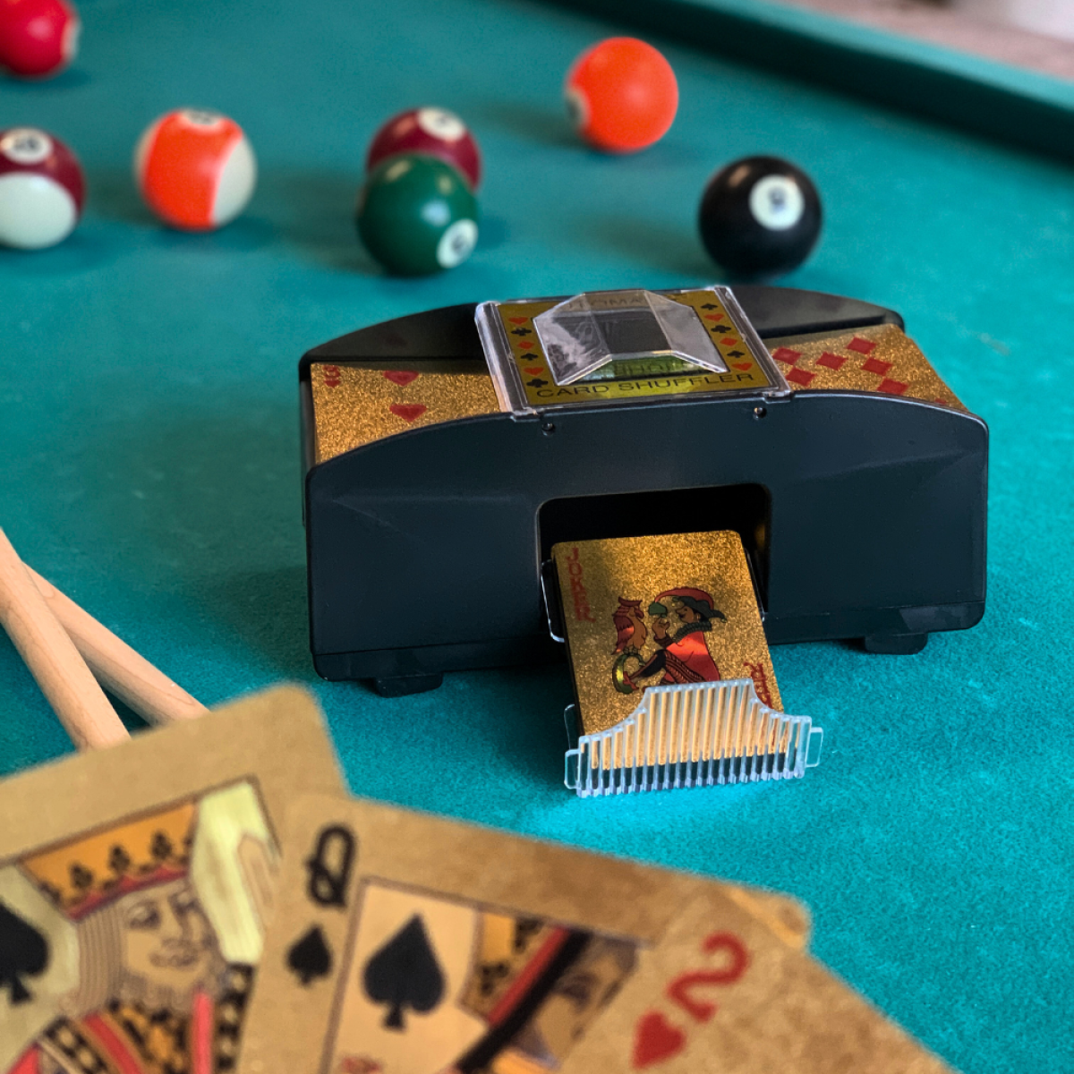Een kaardenschudder op een biljarttafel met poolballen en speelkaarten.