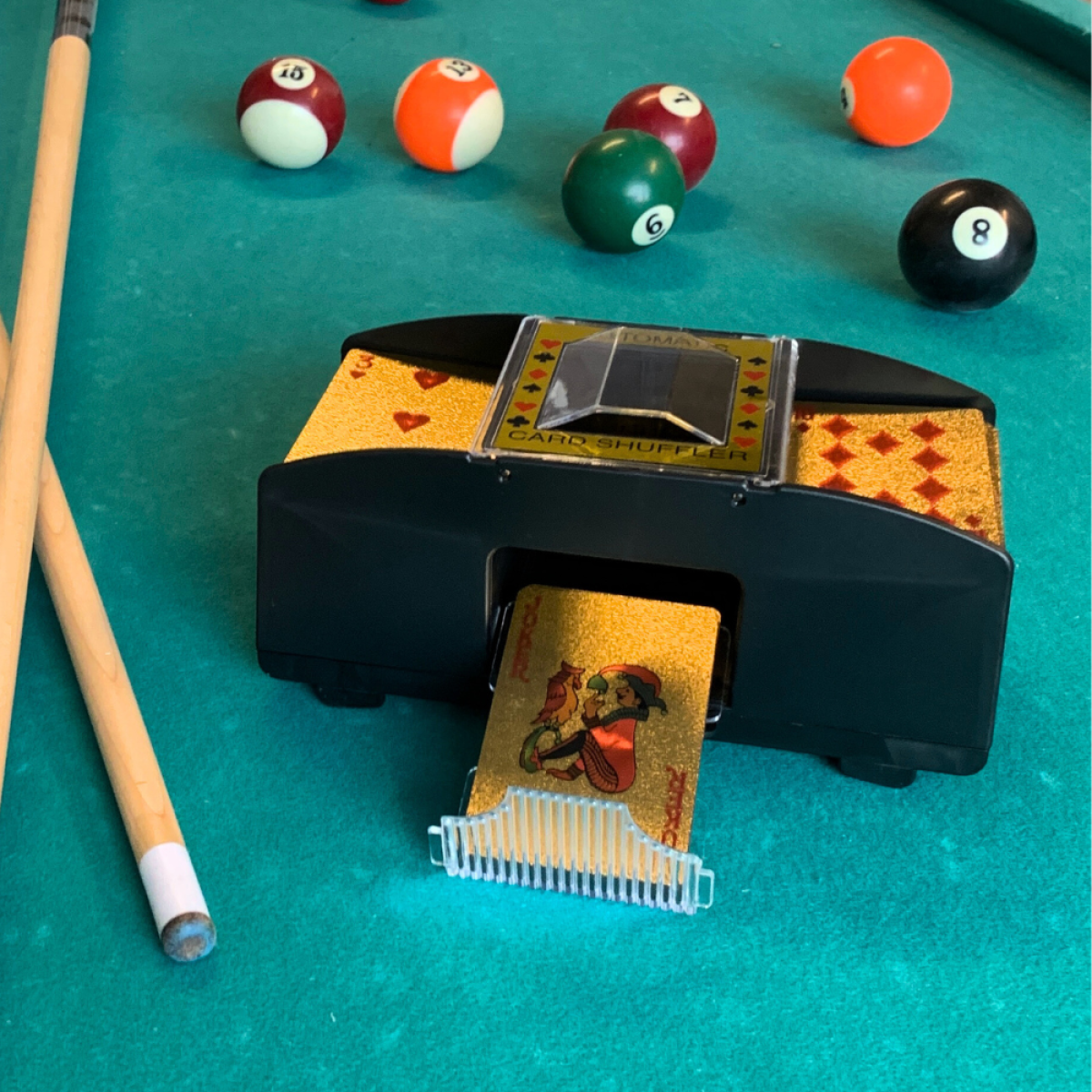 Een kaardenschudmachine met gouden kaarten en biljartballen op groene tafel.