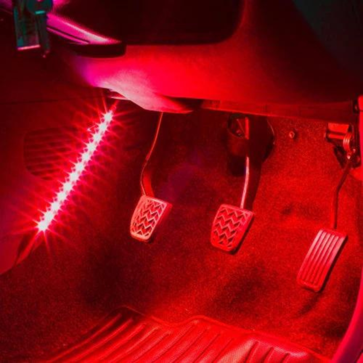 Auto-interieur verlicht met rode LED-strips, drie pedalen zichtbaar.