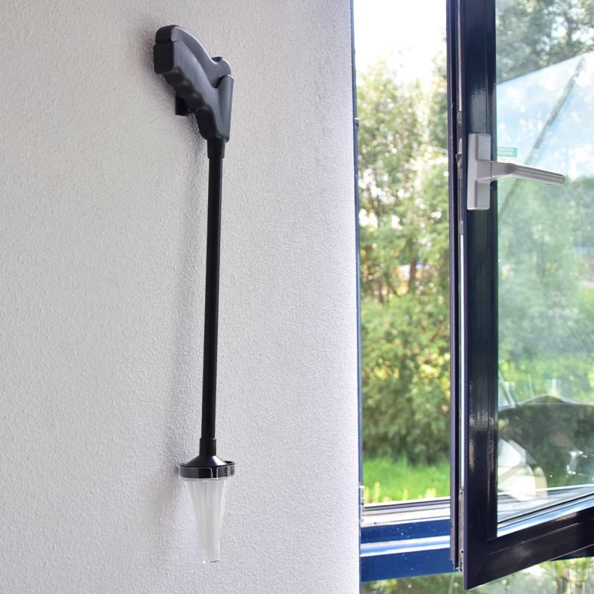 Een zwart schoonmaakapparaat hangt aan een witte muur naast een open raam.