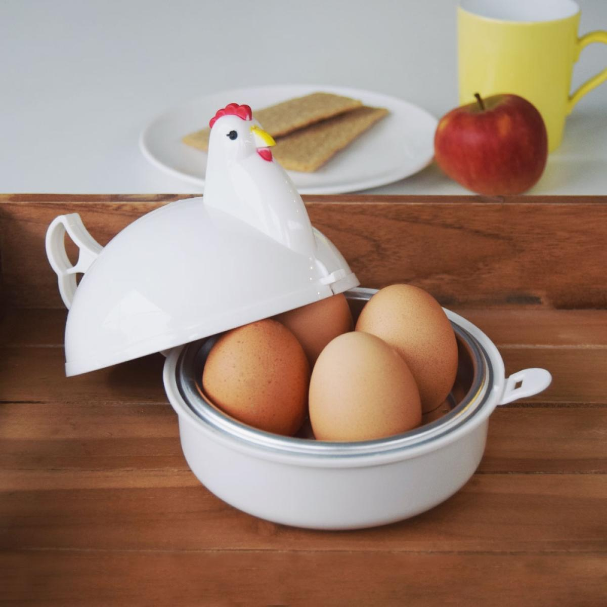 A white chicken egg cooker with eggs inside, next to an apple and crackers.