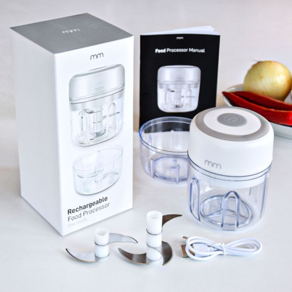 A white mini food processor with accessories and packaging on a white surface.