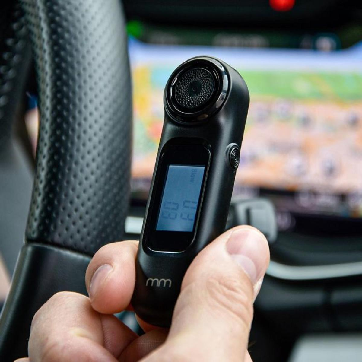 A black device with a display is held near a steering wheel.