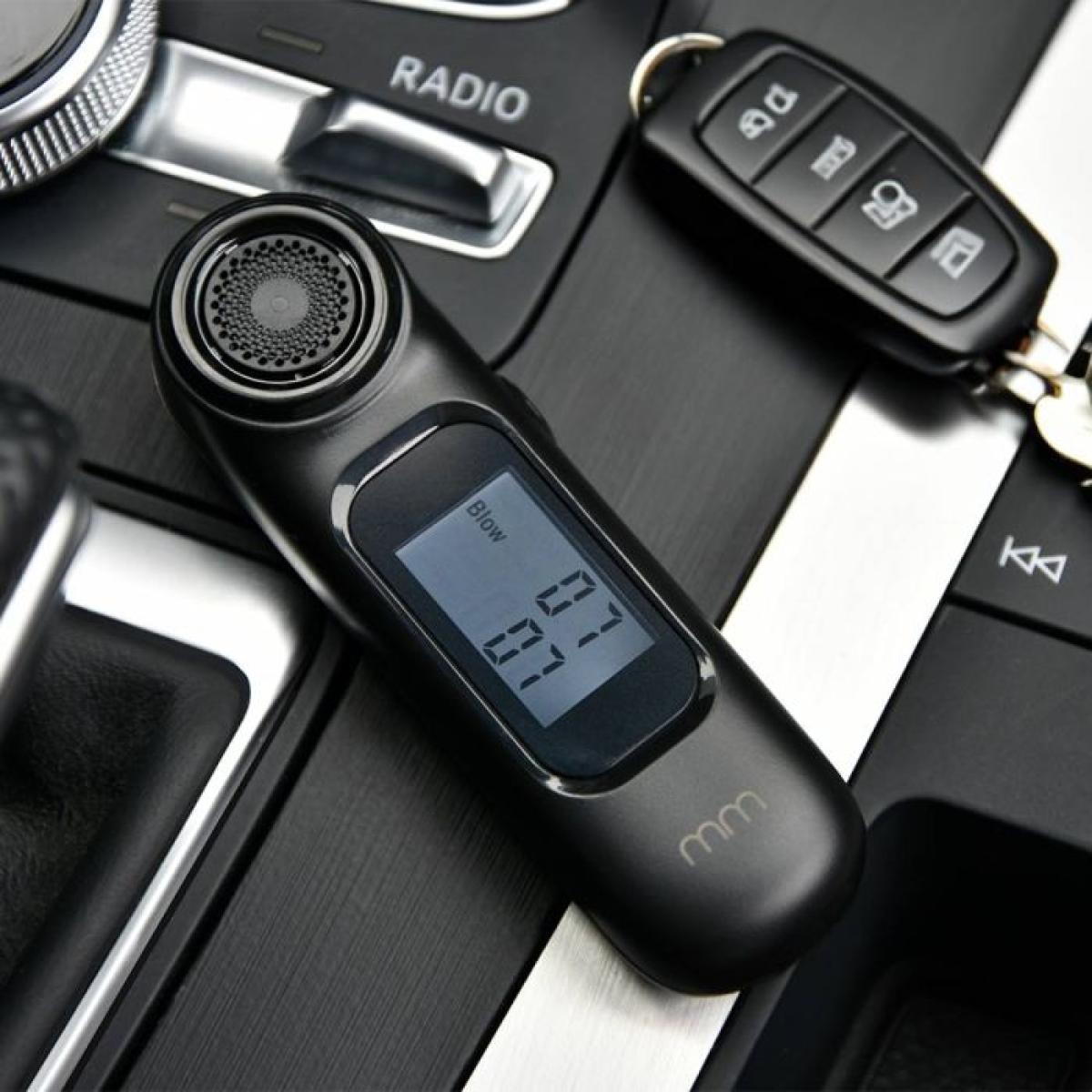 A black breathalyzer rests on a car dashboard next to car keys.
