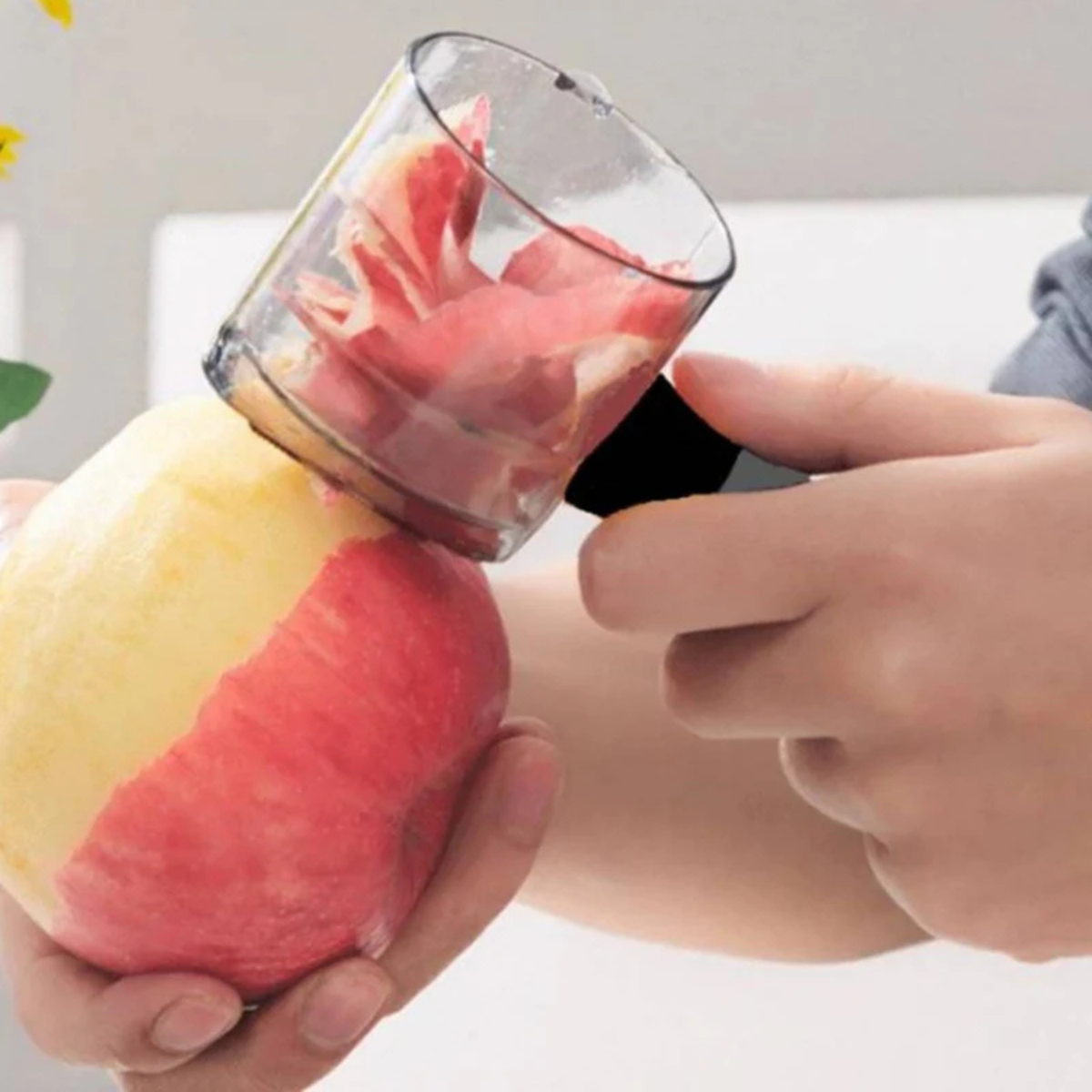 An apple is being peeled with a peeler, the peel collects in the container.