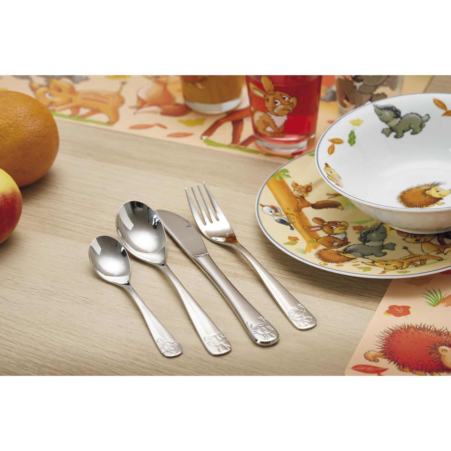 Posate per bambini con animali, frutta e bicchieri su tavolo legno.