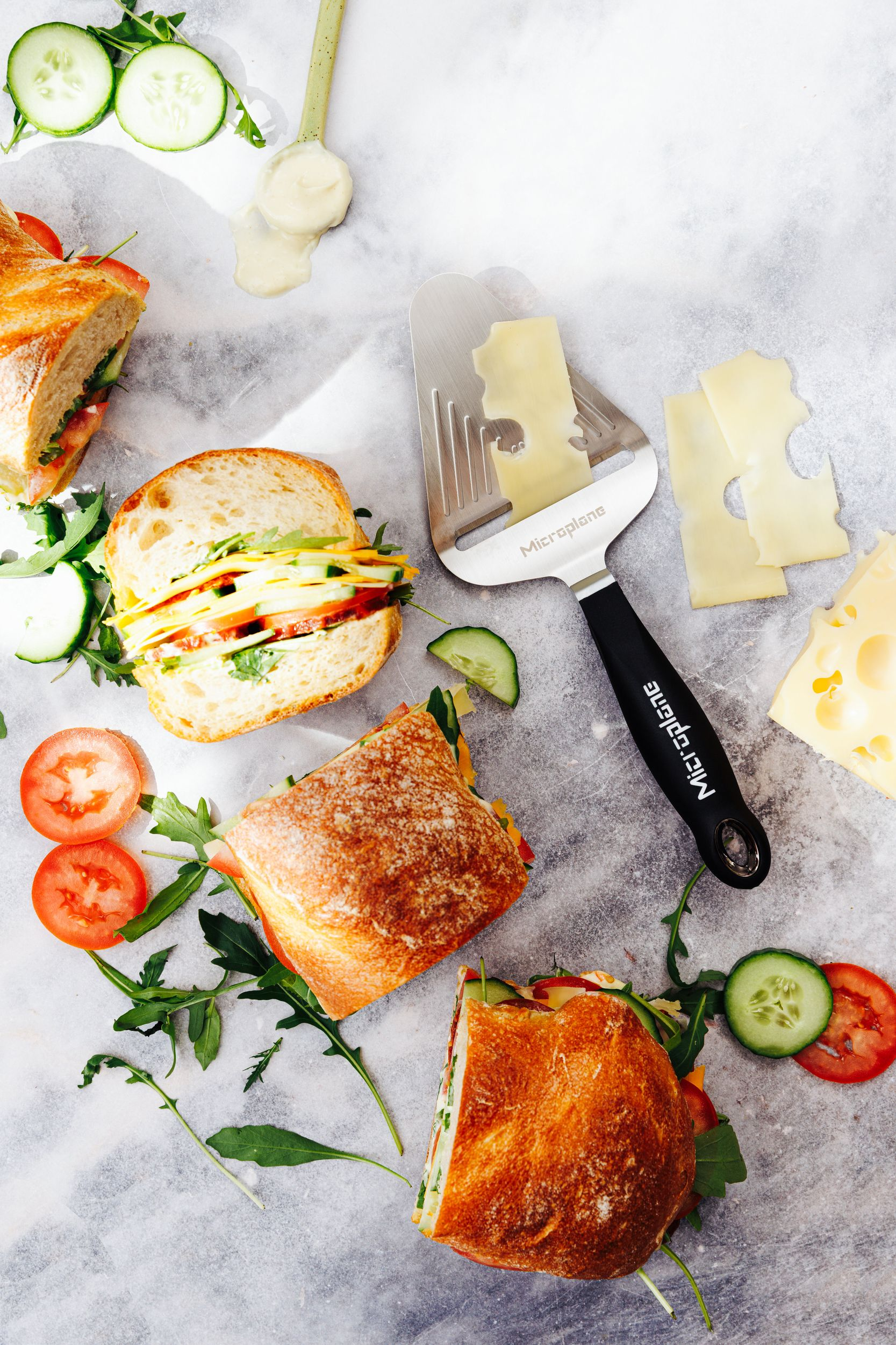 Sandwiches mit Gurke, Tomate, Salat, Käse und einem Käseschneider.