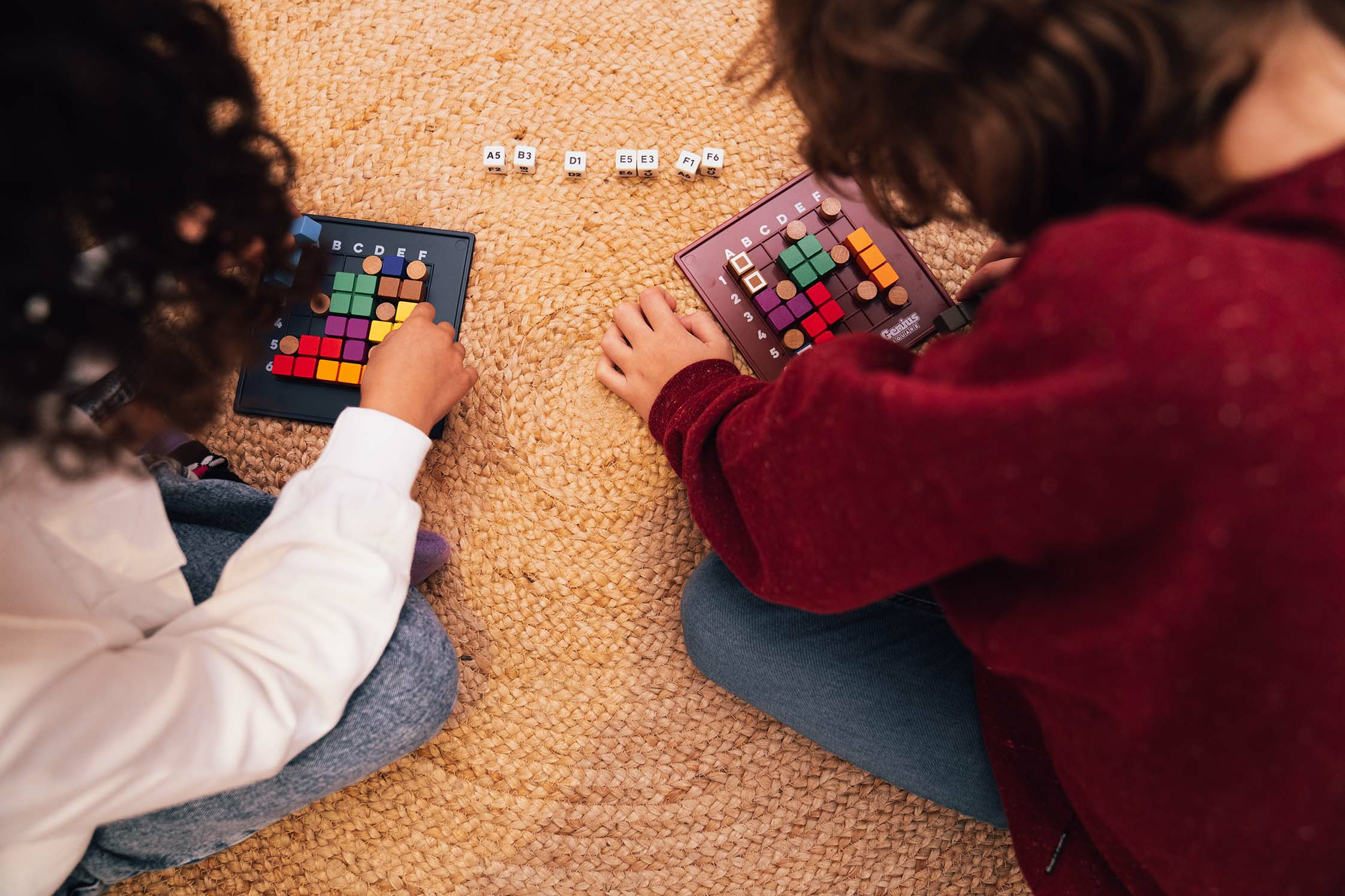 Zwei Kinder spielen Strategiespiele auf einem Teppich mit bunten Blöcken.
