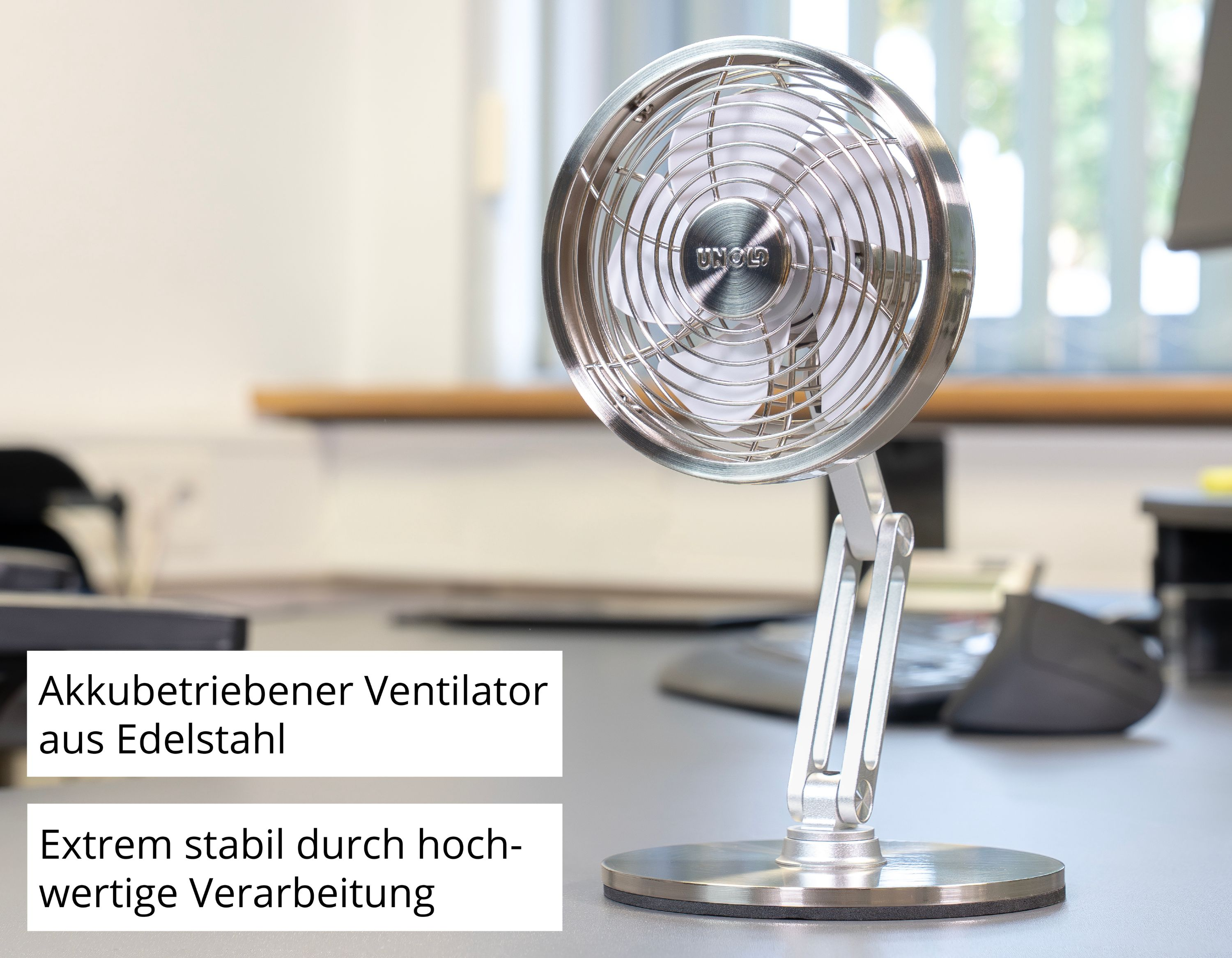 Un ventilatore da tavolo argentato in acciaio inossidabile è su una scrivania.