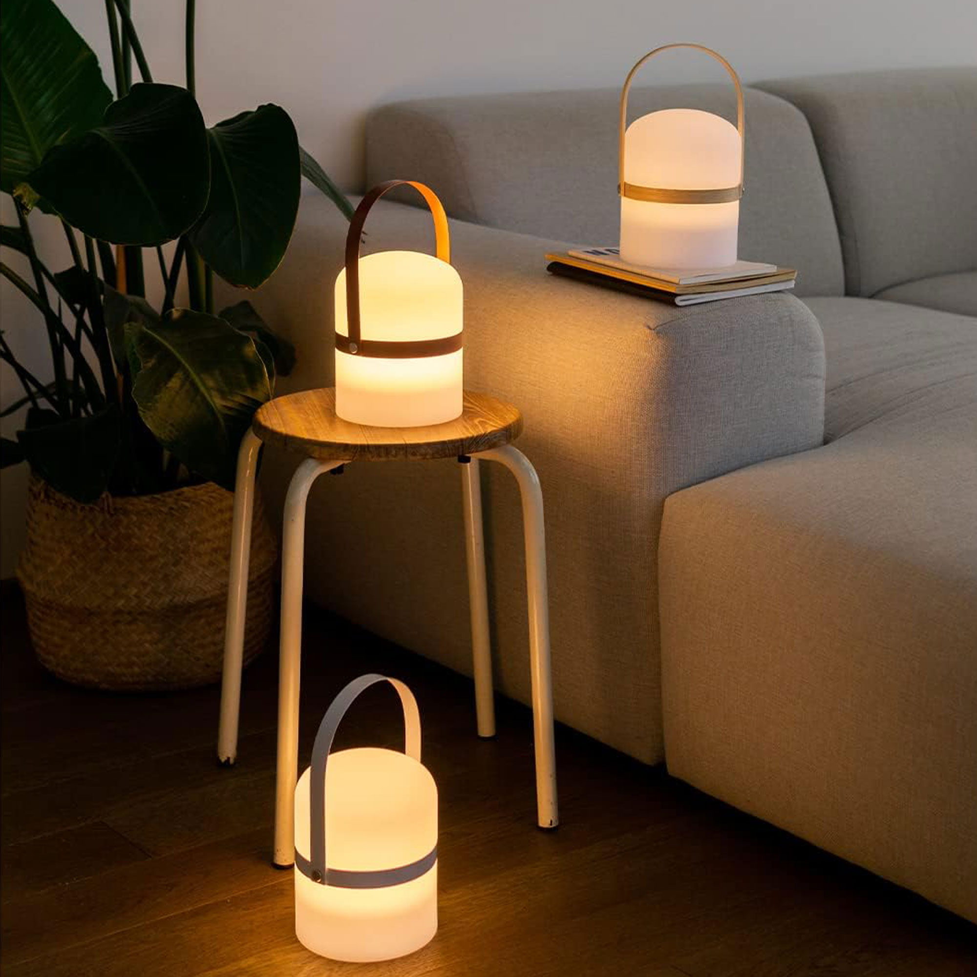 Tres linternas brillantes en una sala de estar junto a un sofá y una planta.