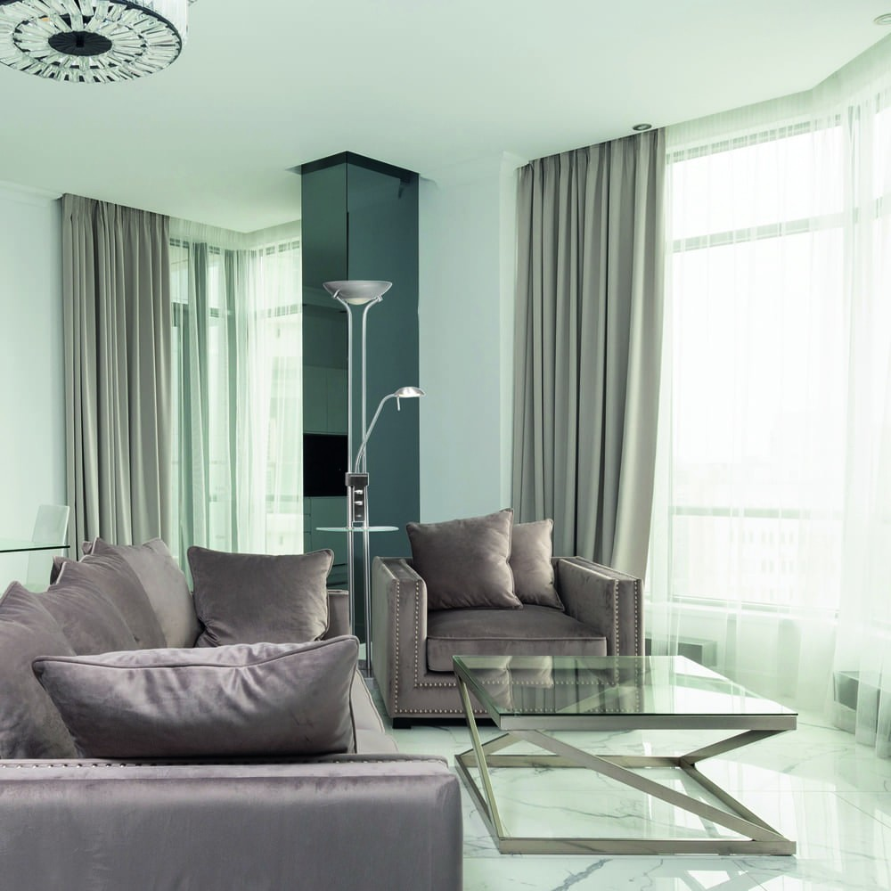 Una sala de estar moderna con sofás grises, mesa de cristal y lámpara de pie.